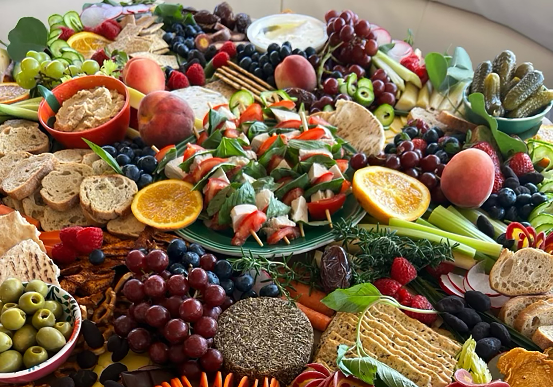 A charcuterie board is displayed with crackers, vegan cheese, olives, fruit and other various vegan treats. 