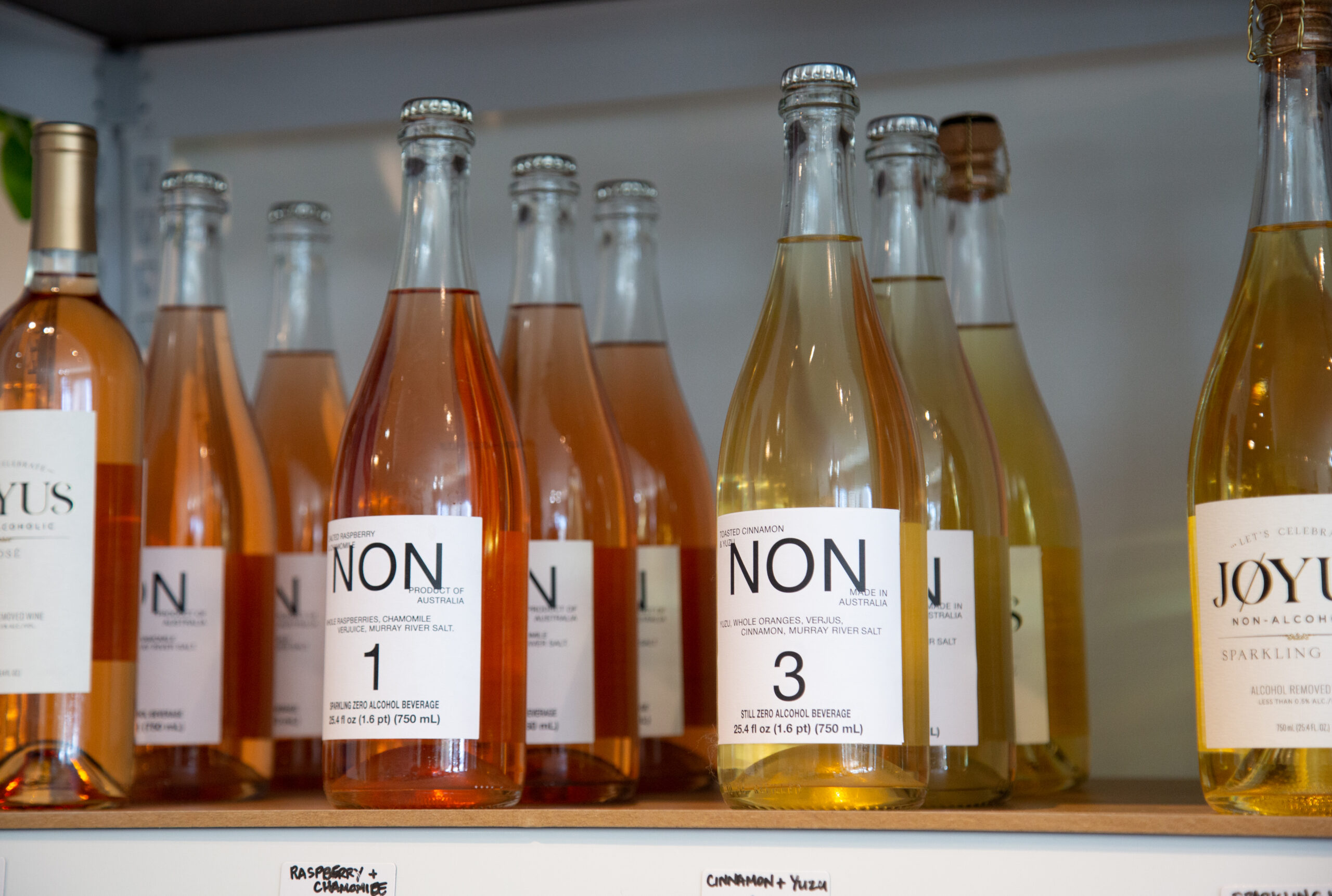 A row of (non-alcoholic) wine bottles sit on a shelf.
